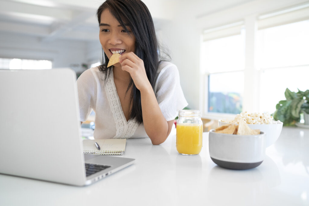 Mulher comendo lanche no trabalho com suco e pipoca, representando escolhas alimentares no cálculo renal