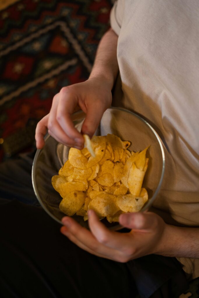 Pessoa comendo salgadinho em pote de vidro, representando consumo de ultraprocessados com alto teor de sal
