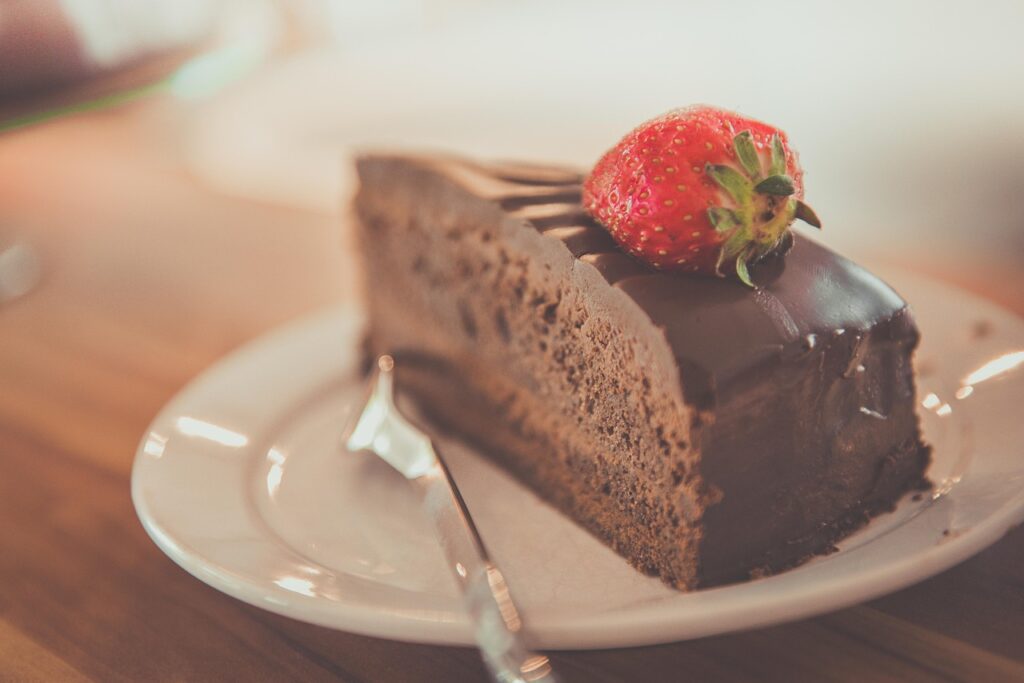 Fatia de bolo de chocolate com cobertura e morango sobre prato branco, ilustrando o consumo moderado de doces para quem tem tendência a cálculos renais.
